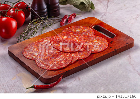 Sliced salami on wooden cutting board with fresh tomatoes and herbs Sliced salami on wooden cutting board with fresh tomatoes and herbs 141317160