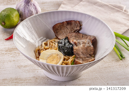 Bowl of ramen with sliced pork, soft boiled egg, nori, and green onions on rustic table with lime and garlic Bowl of ramen with sliced pork, soft boiled egg, nori, and green onions on rustic table with lime and garlic 141317209