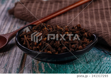 Dried cloves in black bowl with wooden spoon on rustic textured surface 141317293