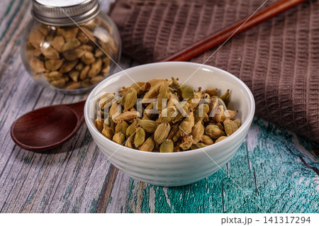Cardamom pods in white ceramic bowl with wooden spoon and glass jar on rustic wood background 141317294