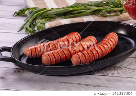 Grilled sausages in black cast iron skillet with green herbs and red sauce Grilled sausages in black cast iron skillet with green herbs and red sauce 141317304