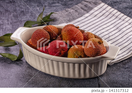 Fresh lychee fruits in white ceramic dish with green leaves on textured gray surface Fresh lychee fruits in white ceramic dish with green leaves on textured gray surface 141317312