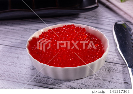 Vibrant red caviar in white ceramic bowl on rustic wooden surface 141317362