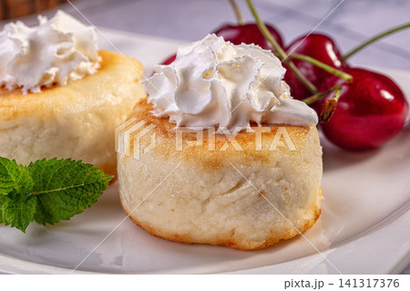 Syrniki with whipped cream and cherries on white plate Syrniki with whipped cream and cherries on white plate 141317376