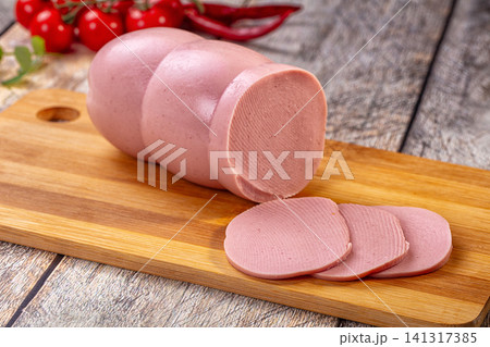 Sliced sausage on wooden cutting board with cherry tomatoes and red chili peppers in background 141317385
