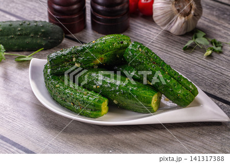 Fresh pickled cucumbers on white plate with garlic and pepper mills on rustic wood Fresh pickled cucumbers on white plate with garlic and pepper mills on rustic wood 141317388