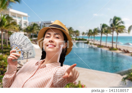 Smiling young Caucasian woman showing dollar bills near a hotel pool during a summer vacation. Travel loan, holiday expenses, vacation budget, and financial planning concept. 141318057
