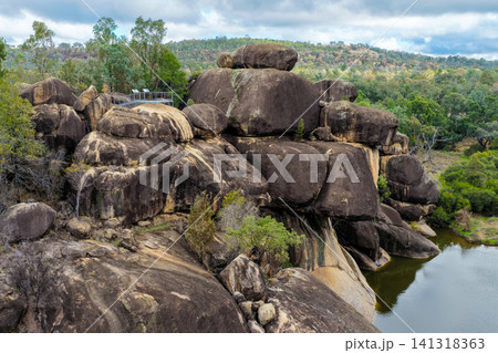 Scenic view of the natural rock pool and impressive granite rock formations at Cranky Rock Nature Reserve near Warialda, NSW. Set beneath a cloudy blue sky and surrounded by native bushland Scenic view of the natural rock pool and impressive granite rock formations at Cranky Rock Nature Reserve near Warialda, NSW. Set beneath a cloudy blue sky and surrounded by native bushland 141318363