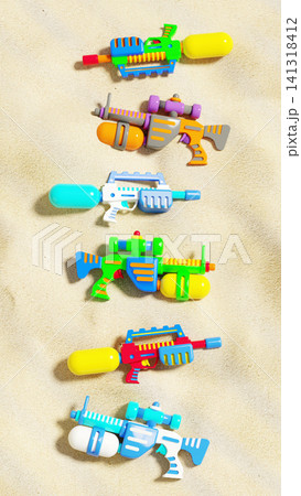 Colorful plastic water guns collection flat lay on sea beach sand, summer vacation background, 3D render 141318412