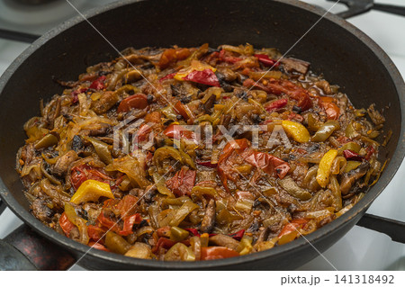 Photo of a roasted vegetable stew in brightly colorful colors on black frying pan. The ingredients consist of mushrooms, tomatoes, lemon, onions, fat, oil, seasonings, bell pepper. Home cooking 141318492