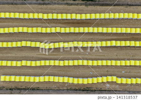 Aerial downward view of rows of wrapped round cotton modules with bright yellow wrap neatly lined up at a cotton gin awaiting transport and processing. Aerial downward view of rows of wrapped round cotton modules with bright yellow wrap neatly lined up at a cotton gin awaiting transport and processing. 141318537