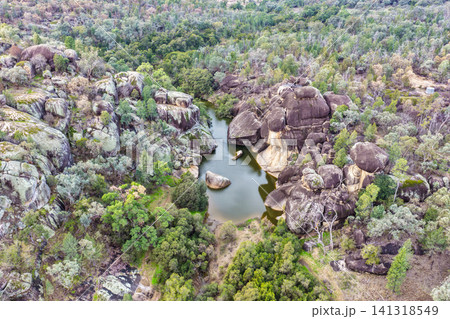 Scenic view of the natural rock pool and impressive granite rock formations at Cranky Rock Nature Reserve near Warialda, NSW. Set beneath a cloudy blue sky and surrounded by native bushland Scenic view of the natural rock pool and impressive granite rock formations at Cranky Rock Nature Reserve near Warialda, NSW. Set beneath a cloudy blue sky and surrounded by native bushland 141318549