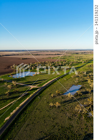 Aerial vertical scene showcasing cultivated farmland with a rural dirt road connecting to a main road, scattered farm dams and a lush green landscape near Pilliga, highlighting the striking patterns Aerial vertical scene showcasing cultivated farmland with a rural dirt road connecting to a main road, scattered farm dams and a lush green landscape near Pilliga, highlighting the striking patterns 141319232
