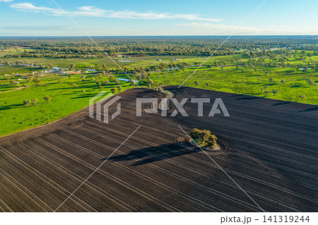 Aerial view showcasing cultivated farmland with striking natural patterns in the foreground, while the Pilliga Artesian Bore Baths and campground sit amongst a lush green landscape in the background Aerial view showcasing cultivated farmland with striking natural patterns in the foreground, while the Pilliga Artesian Bore Baths and campground sit amongst a lush green landscape in the background 141319244