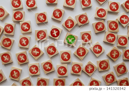 Overhead flat lay view of a single green tick check mark on a wooden cube surrounded by many blocks with red cross reject symbols on a white background Overhead flat lay view of a single green tick check mark on a wooden cube surrounded by many blocks with red cross reject symbols on a white background 141320342