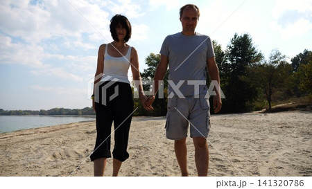 Romantic couple holding hands of each other and walking at coastline. Happy pair going along seashore at sunny day. Lovers spending time together at resort. Concept of vacation or holiday. Slow motion Romantic couple holding hands of each other and walking at coastline. Happy pair going along seashore at sunny day. Lovers spending time together at resort. Concept of vacation or holiday. Slow motion 141320786
