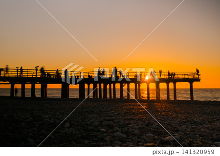 View of silhouettes of people walk on the pier against dramatic sunset sky View of silhouettes of people walk on the pier against dramatic sunset sky 141320959