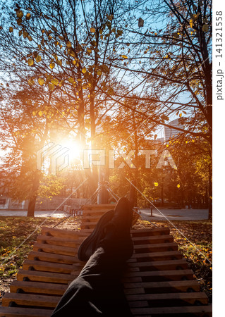 person resting in wooden hammock or bench in autumn park at sunset person resting in wooden hammock or bench in autumn park at sunset 141321558