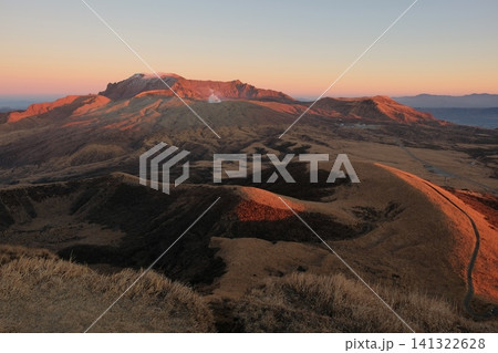 夕闇に沈む草原と夕日に赤く染まる冬の阿蘇山高岳の連峰風景 141322628