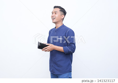 Young man holds wallet, surprised expression. Blue shirt and jeans complete casual look. Blank white background ensures clean focus. Emotion conveys shock or disbelief. Ideal for finance Young man holds wallet, surprised expression. Blue shirt and jeans complete casual look. Blank white background ensures clean focus. Emotion conveys shock or disbelief. Ideal for finance 141323117