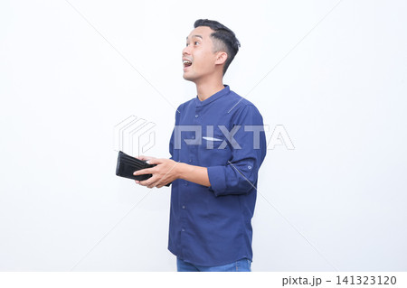 Young man holds wallet, surprised expression. Blue shirt and jeans complete casual look. Blank white background ensures clean focus. Emotion conveys shock or disbelief. Ideal for finance Young man holds wallet, surprised expression. Blue shirt and jeans complete casual look. Blank white background ensures clean focus. Emotion conveys shock or disbelief. Ideal for finance 141323120