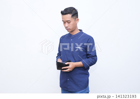 Young man holds wallet, touches forehead in stress. He wears blue shirt, shows frustration or disappointment. Blank background emphasizes emotional moment. Ideal for financial struggles Young man holds wallet, touches forehead in stress. He wears blue shirt, shows frustration or disappointment. Blank background emphasizes emotional moment. Ideal for financial struggles 141323193