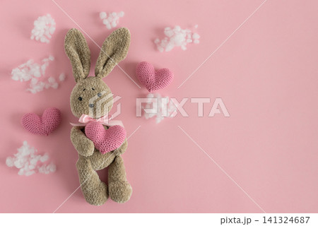Stuffed bunny holding heart on pink background Stuffed bunny holding heart on pink background 141324687