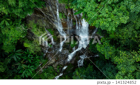 Aerial view of deep tropical rainforest with waterfall surrounded by lush tropical forest and towering cliffs streams of water into deep canyon, Lush green trees in forest with natural stream. Aerial view of deep tropical rainforest with waterfall surrounded by lush tropical forest and towering cliffs streams of water into deep canyon, Lush green trees in forest with natural stream. 141324852