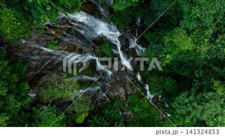 Aerial view of deep tropical rainforest with waterfall surrounded by lush tropical forest and towering cliffs streams of water into deep canyon, Lush green trees in forest with natural stream. 141324853