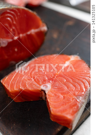 Closeup of two raw smoked sockeye salmon steaks on dark wooden board with vivid orange flesh and moist texture Closeup of two raw smoked sockeye salmon steaks on dark wooden board with vivid orange flesh and moist texture 141325105
