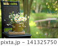 Brass retro teapot with daisies and an old book on a chair 141325750