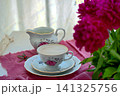A bouquet of burgundy peonies, a coffee cup, and a porcelain set. 141325756