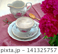 A bouquet of burgundy peonies, a coffee cup, and a porcelain set. 141325757