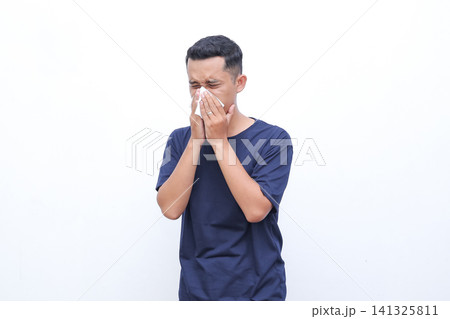 Man wipes nose with tissue. He looks distressed or ill. Simple background highlights his action. Perfect for allergy or flu related content. Use in health, wellness, or medical contexts 141325811