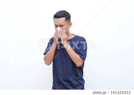 Man wipes nose with tissue. He looks distressed or ill. Simple background highlights his action. Perfect for allergy or flu related content. Use in health, wellness, or medical contexts 141325812