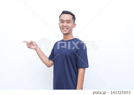 Young man smiles, pointing left with open palm. Simple navy tee, clean white background. Friendly gesture suggests product or idea. Ideal for advertising, presentations, or promotions Young man smiles, pointing left with open palm. Simple navy tee, clean white background. Friendly gesture suggests product or idea. Ideal for advertising, presentations, or promotions 141325853