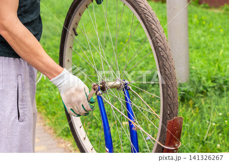 Man fixing bicycle wheel at doorstep. Own vehicle maintenance without service center. Responsible ownership visible. Summer commute switched to pedal power Man fixing bicycle wheel at doorstep. Own vehicle maintenance without service center. Responsible ownership visible. Summer commute switched to pedal power 141326267