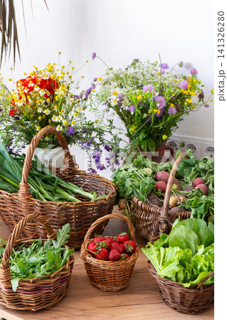 Freshly picked organic vegetables and strawberries are arranged in woven baskets on a wooden table. These local harvests show vibrant greens and red strawberries in a sunny setting Freshly picked organic vegetables and strawberries are arranged in woven baskets on a wooden table. These local harvests show vibrant greens and red strawberries in a sunny setting 141326280