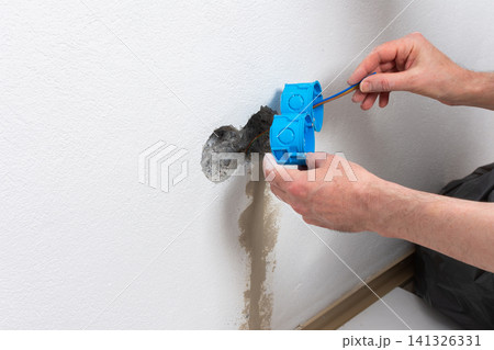Skilled electrician carefully places blue flush-mount boxes into a wall opening, preparing for a new double electrical outlet installation in an apartment during home improvement 141326331
