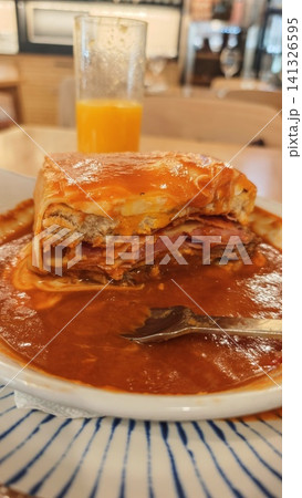 Layered lasagna with meat, cheese, and sauce served on a plate, accompanied by a glass of orange juice in a casual dining setting 141326595
