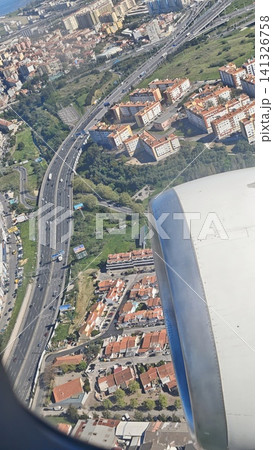 Aerial perspective showing a mix of residential buildings and highways below, with an airplane wing prominently displayed in the foreground Aerial perspective showing a mix of residential buildings and highways below, with an airplane wing prominently displayed in the foreground 141326758