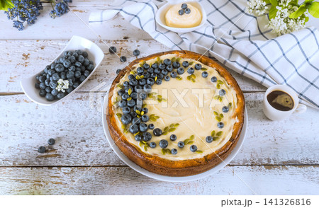 Blueberry cheesecake on table with dessert toppings fresh berries in kitchen setting Blueberry cheesecake on table with dessert toppings fresh berries in kitchen setting 141326816