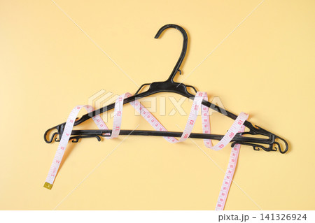 A measuring tape around Clothes hanger on color background, top view. A measuring tape around Clothes hanger on color background, top view. 141326924