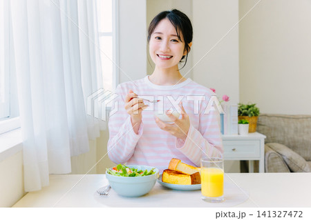 朝食でヨーグルトを食べる若い女性 朝食でヨーグルトを食べる若い女性 141327472