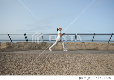 Woman jogging along seaside promenade for fitness and healthy lifestyle Woman jogging along seaside promenade for fitness and healthy lifestyle 141327780