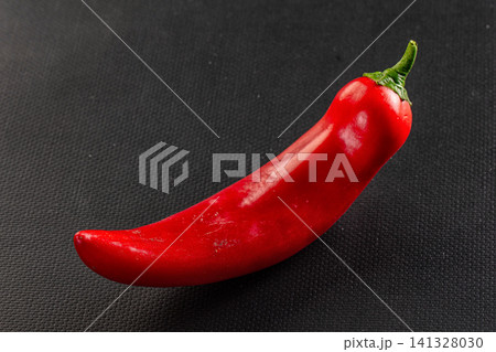 Vibrant red chili pepper on dark textured surface Vibrant red chili pepper on dark textured surface 141328030