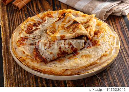 Golden crepes stacked on ceramic plate with cinnamon sticks on rustic wood Golden crepes stacked on ceramic plate with cinnamon sticks on rustic wood 141328042