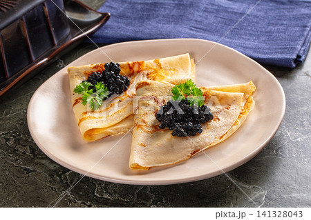 Crepes with black caviar and parsley on ceramic plate 141328043
