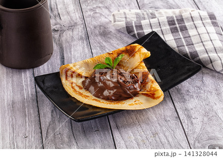 Folded crepe with chocolate spread and mint on black plate Folded crepe with chocolate spread and mint on black plate 141328044