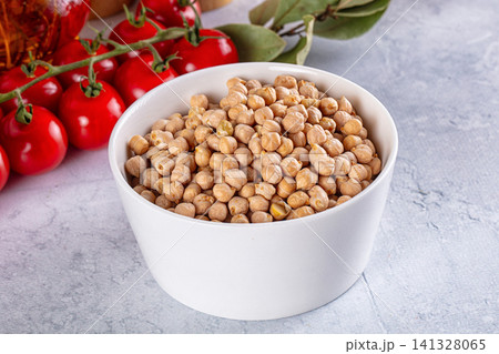 White bowl filled with chickpeas beside cherry tomatoes and bay leaves on textured surface White bowl filled with chickpeas beside cherry tomatoes and bay leaves on textured surface 141328065